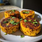 Four golden-brown Spicy Jamaican Lentil Quinoa Vegan Patties topped with fresh cilantro, served on a white plate.