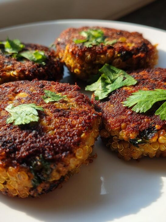 Four golden-brown Spicy Jamaican Lentil Quinoa Vegan Patties garnished with fresh cilantro on a white plate.