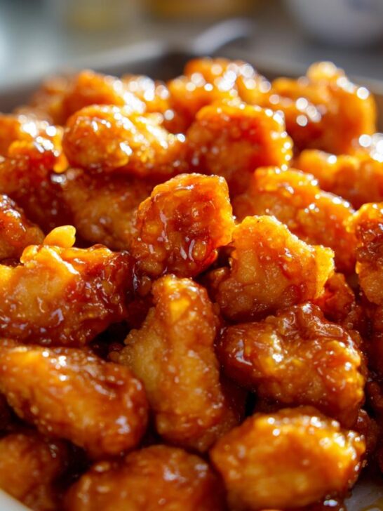 A close-up, mouthwatering shot of Sticky Orange Chicken Popcorn Chicken coated in a glistening orange sauce.