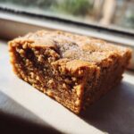 A close-up, sunlit shot of a single, thick square of Peanut Butter Cookie Bars topped with sparkling sugar crystals.