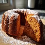 A delicious Sweet Potato Bundt Cake dusted with powdered sugar, with a slice removed to show the moist interior.