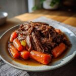 A plate of shredded Ultimate Slow Cooker Pot Roast with tender carrots in rich gravy.
