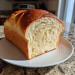 A golden-brown loaf of vegan brioche bread, sliced to show its soft, airy crumb.