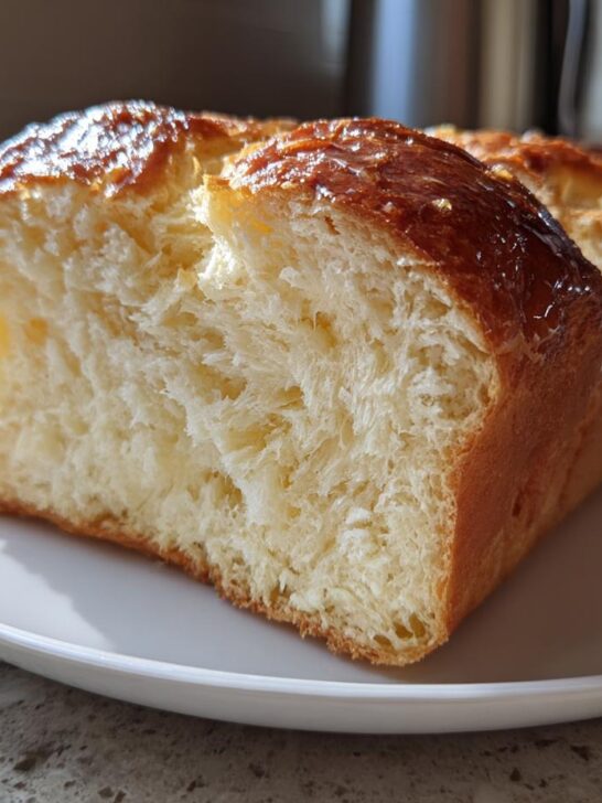 A close-up of a slice of fluffy Vegan Brioche Bread on a white plate, showcasing its soft texture and golden-brown crust.