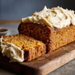 A slice of moist Vegan Pumpkin Bread topped with creamy Maple Chai Frosting on a wooden board.