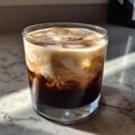 A close-up shot of a White Russian cocktail with ice, showing the creamy swirls of Kahlua and vodka.