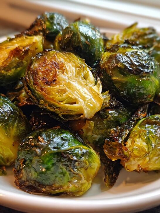 A close-up of perfectly cooked, slightly charred Air Fryer Brussels Sprouts piled high in a white bowl.