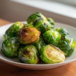 A close-up of perfectly cooked Air Fryer Brussels Sprouts piled high on a light-colored plate, showing crispy, browned edges.