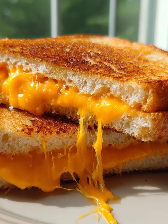 Two halves of a golden brown Air Fryer Grilled Cheese sandwich stacked, with bright orange cheese oozing out and stretching downwards.