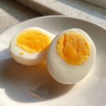 Two halves of a perfectly cooked Air Fryer Hard Boiled Eggs showing a firm, bright yellow yolk on a white plate.