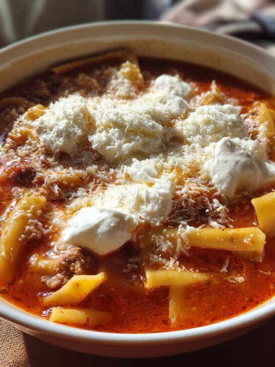 A close-up of a hearty bowl of Lasagna Soup featuring rich tomato broth, pasta pieces, ground meat, and topped with dollops of ricotta and grated Parmesan cheese.