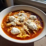 A close-up of a hearty bowl of Lasagna Soup featuring ruffled pasta, rich tomato broth, and dollops of ricotta cheese.