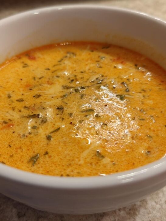 Close-up of a white bowl filled with creamy Apple Cheddar Sweet Potato Soup, garnished with herbs.