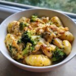 Close-up of a bowl filled with Baked Garlic Chicken Broccoli Gnocchi Recipe, topped with melted cheese and herbs.