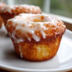 Close-up of a golden brown Baked Vanilla Glazed Donut Muffin with thick white icing dripping down the sides.