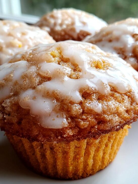 Four golden Baked Vanilla Glazed Donut Muffins topped with thick white vanilla icing on a white plate.