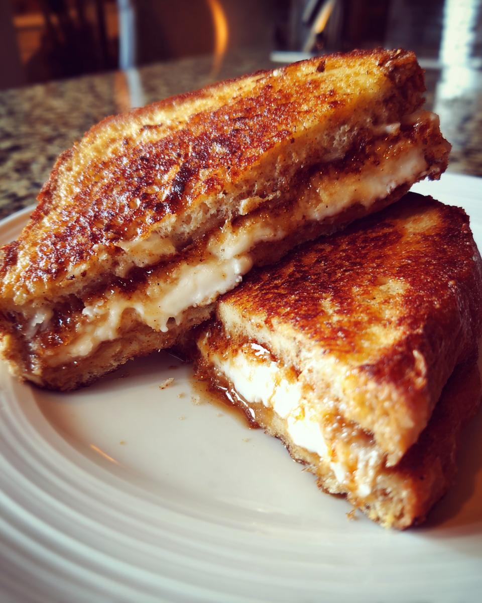 Two halves of golden-brown Banana Bread Stuffed French Toast stacked on a white plate, showing creamy filling.