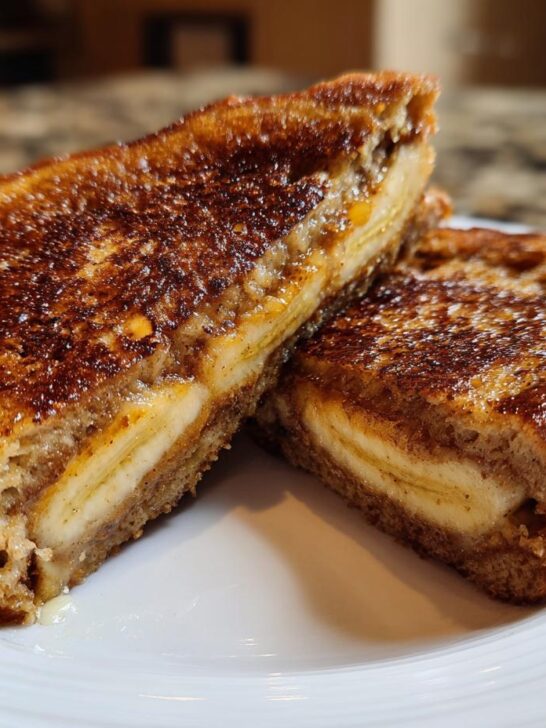 Two halves of golden-brown Banana Bread Stuffed French Toast showing creamy filling and caramelized edges.