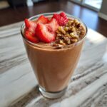 A thick, chocolate-colored Banana Split Smoothie topped with fresh sliced strawberries and walnuts.