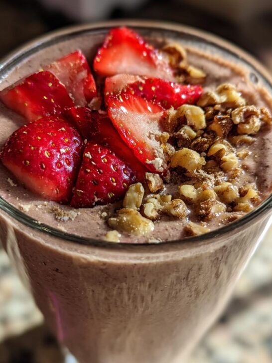 Close-up of a thick Banana Split Smoothie topped with fresh sliced strawberries and chopped walnuts.