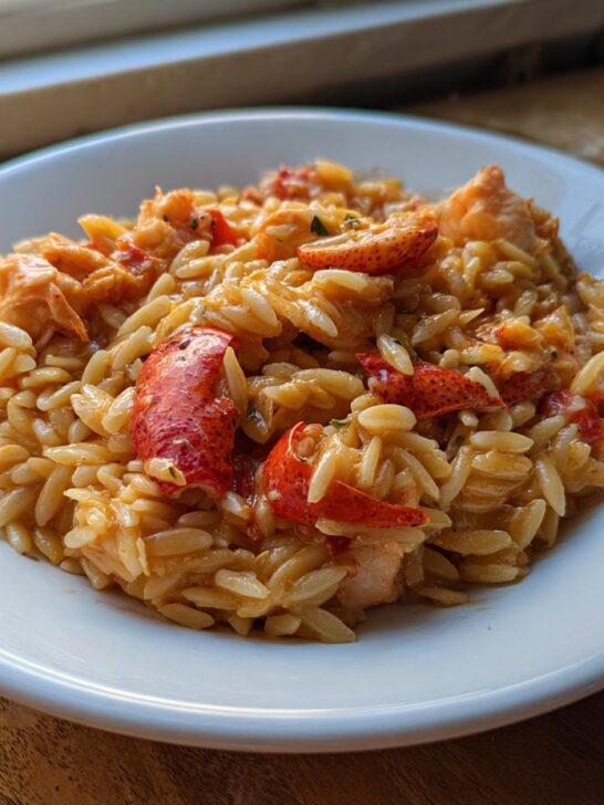 A close-up of BBQ Jerk Lobster Garlic Herb Orzo served on a white plate, featuring bright red lobster pieces mixed with creamy pasta.