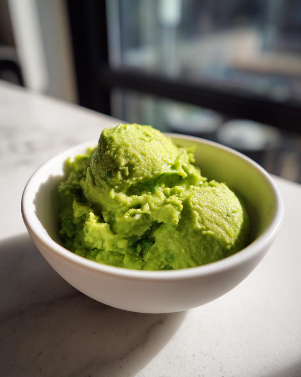 A close-up of creamy, bright green The Best Guacamole scooped into a small white bowl.