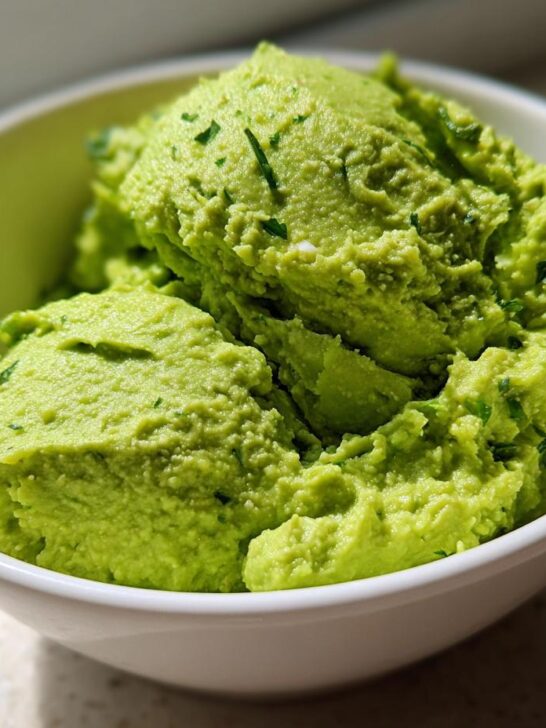 A close-up of creamy, bright green The Best Guacamole scooped into a white bowl, flecked with herbs.
