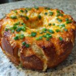 Close-up of a golden-brown Bread Ring Cheese Dip, melted cheese oozing, topped with fresh green chives.