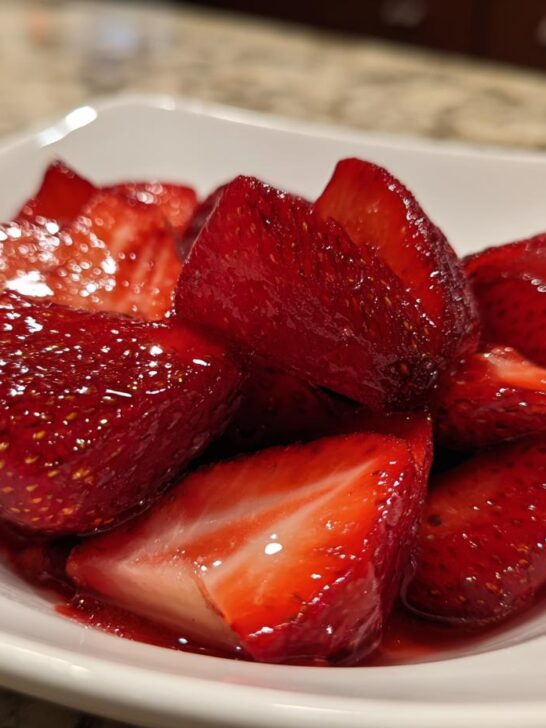 Close-up of glistening, macerated Champagne Strawberries served in a small white bowl.