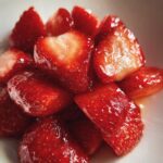 Close-up of glistening, sliced Champagne Strawberries piled in a white bowl, showing their juicy texture.