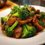A close-up of glossy, saucy Chinese Chicken And Broccoli served on a white plate.