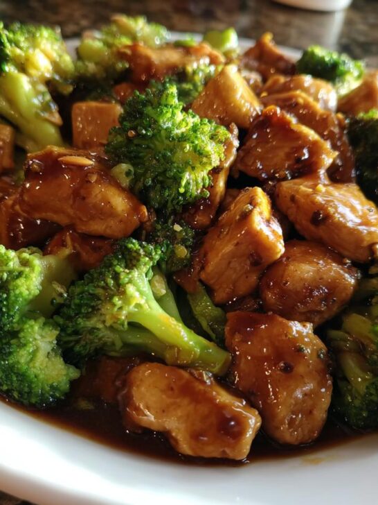A close-up shot of savory Chinese Chicken And Broccoli served on a white plate, coated in a rich brown sauce.