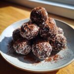 A stack of homemade Chocolate Coconut Energy Bites rolled in shredded coconut and cocoa powder on a light plate.