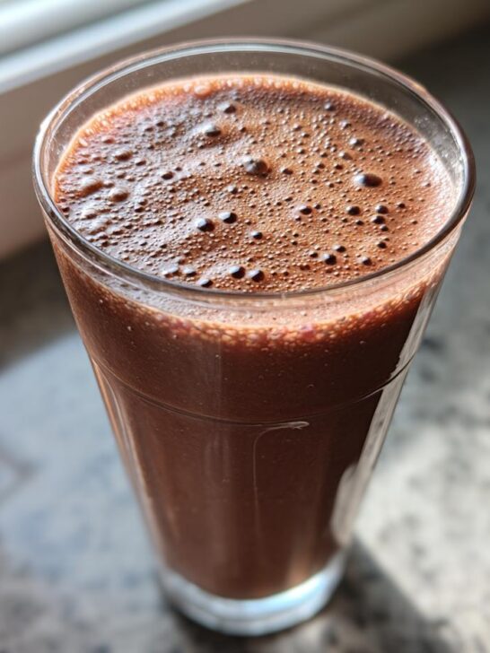 A tall glass filled with a thick, dark brown Chocolate Raspberry Smoothie, showing foam bubbles on top.