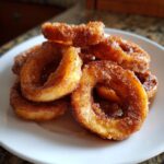 Close-up of several warm, cinnamon-sugar coated Apple Rings piled high on a white plate.