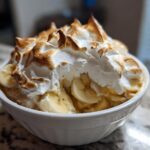 A close-up of Classic Southern Banana Pudding topped with peaks of toasted meringue and sliced bananas in a white bowl.