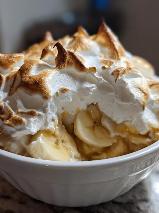 A close-up of Classic Southern Banana Pudding topped with peaks of toasted meringue and sliced bananas in a white bowl.