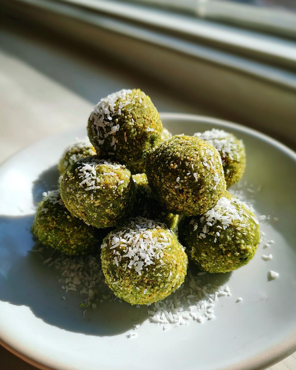 A stack of vibrant green Coconut Matcha Energy Bites rolled in shredded coconut, sitting on a white plate.