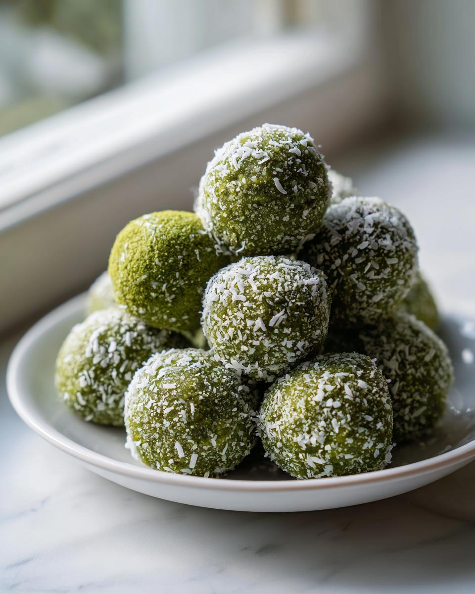 A stack of bright green Coconut Matcha Energy Bites coated in shredded coconut on a white plate.