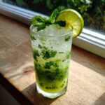 A tall glass filled with crushed ice, mint leaves, and a lime slice, showcasing the Coconut Mojito Mocktail With Green Tea.
