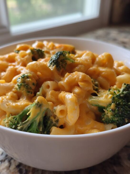 A white bowl filled with creamy Copycat Velveeta Broccoli Mac Cheese, featuring elbow macaroni and bright green broccoli florets.