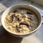 A close-up of a white bowl filled with creamy Cream Of Mushroom Soup With Rice, topped with sliced mushrooms.