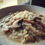 A close-up of a bowl of creamy Cream Of Mushroom Soup With Rice, topped with white rice and sliced mushrooms.