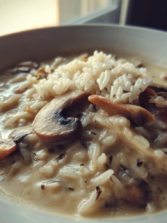 A close-up of a bowl of creamy Cream Of Mushroom Soup With Rice, topped with white rice and sliced mushrooms.