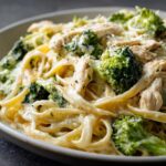 A close-up view of a bowl filled with Creamy Broccoli Chicken Alfredo pasta, featuring fettuccine, sliced chicken, and bright green broccoli florets.