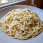 A close-up of a generous serving of Creamy Garlic Alfredo Pasta coated in rich white sauce and topped with grated Parmesan cheese.