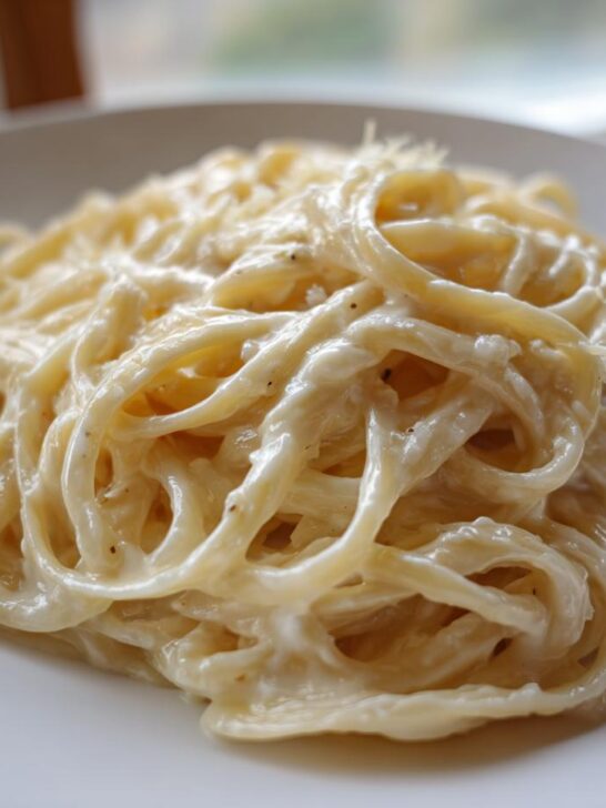 Close-up of a serving of rich, white Creamy Garlic Alfredo Pasta coated in sauce on a white plate.
