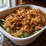 A close-up of a white baking dish filled with baked Creamy Green Bean Casserole topped with crispy fried onions.