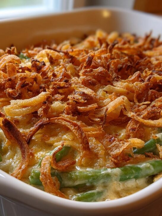 Close-up of a baked Creamy Green Bean Casserole in a white dish, featuring green beans in a creamy sauce and topped with crispy fried onions.
