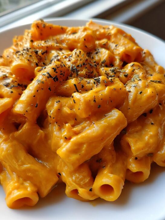 Close-up of rigatoni pasta coated in a rich, orange Creamy Roasted Butternut Squash Pasta sauce, topped with dried herbs.